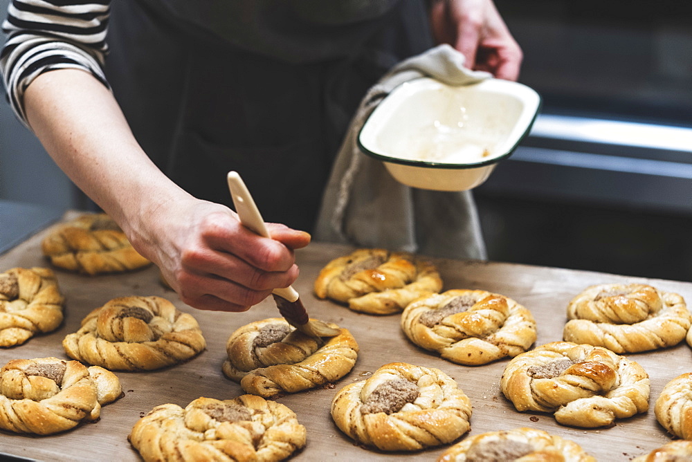 Baker with a pastry brush adding glaze to a tray of cinnamon buns ready for the oven