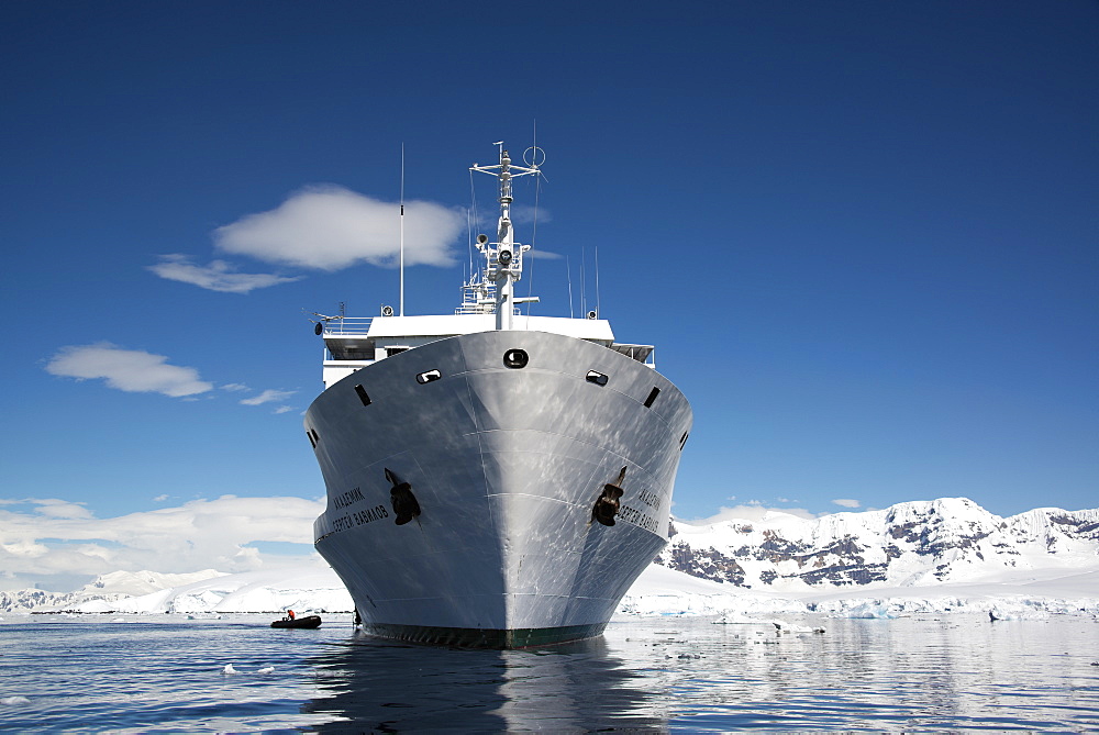 An Antarctic cruise ship with inflatable zodiacs on the calm waters among ice floes and mountainous landscape, Antarctic peninsula, Antarctica