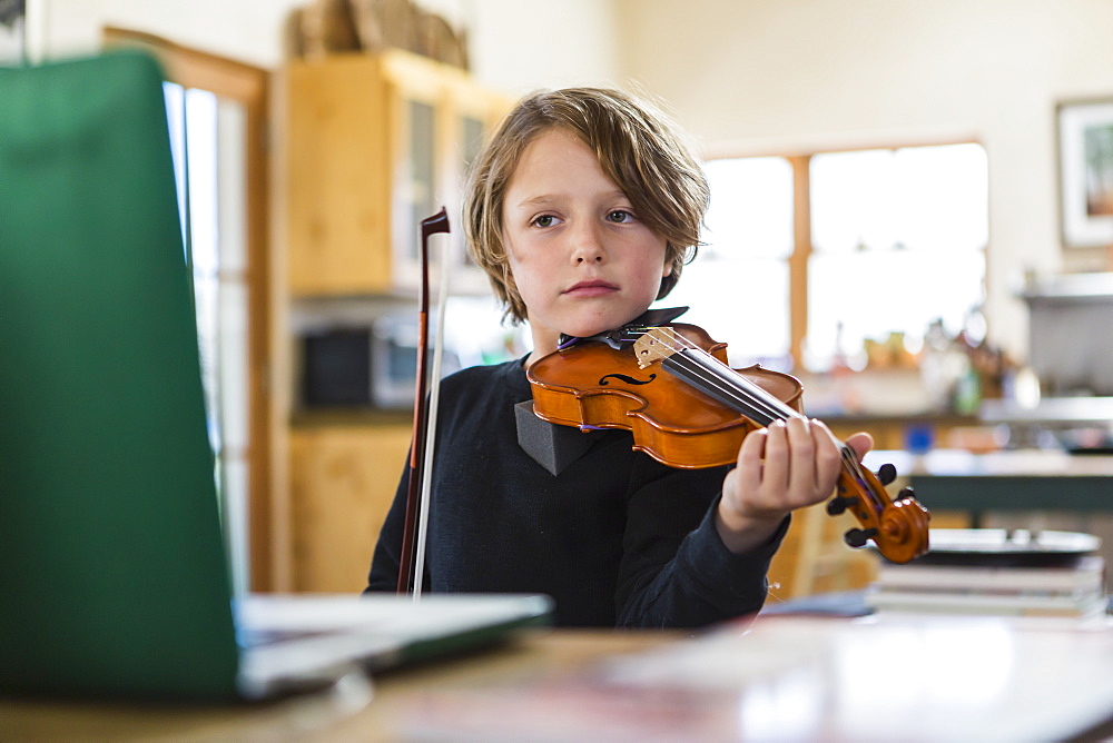 Six year old boy playing violin, having a remote video lesson in lockdown at home