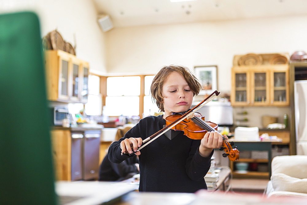 Six year old boy playing violin, having a remote video lesson in lockdown at home