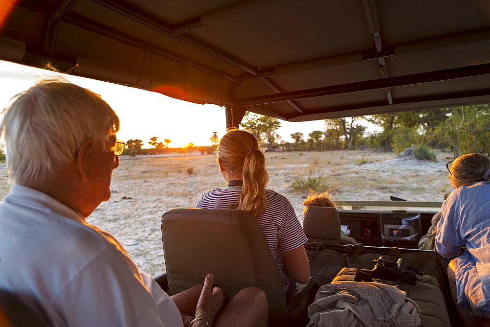 Three generations of a family on safari, in a jeep out at sunset, Moremi Game Reserve, Botswana