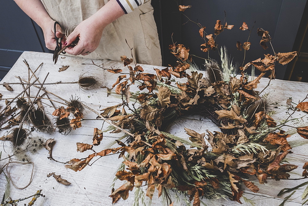 Woman making a small winter wreath of dried plants, brown leaves and twigs, and seedheads