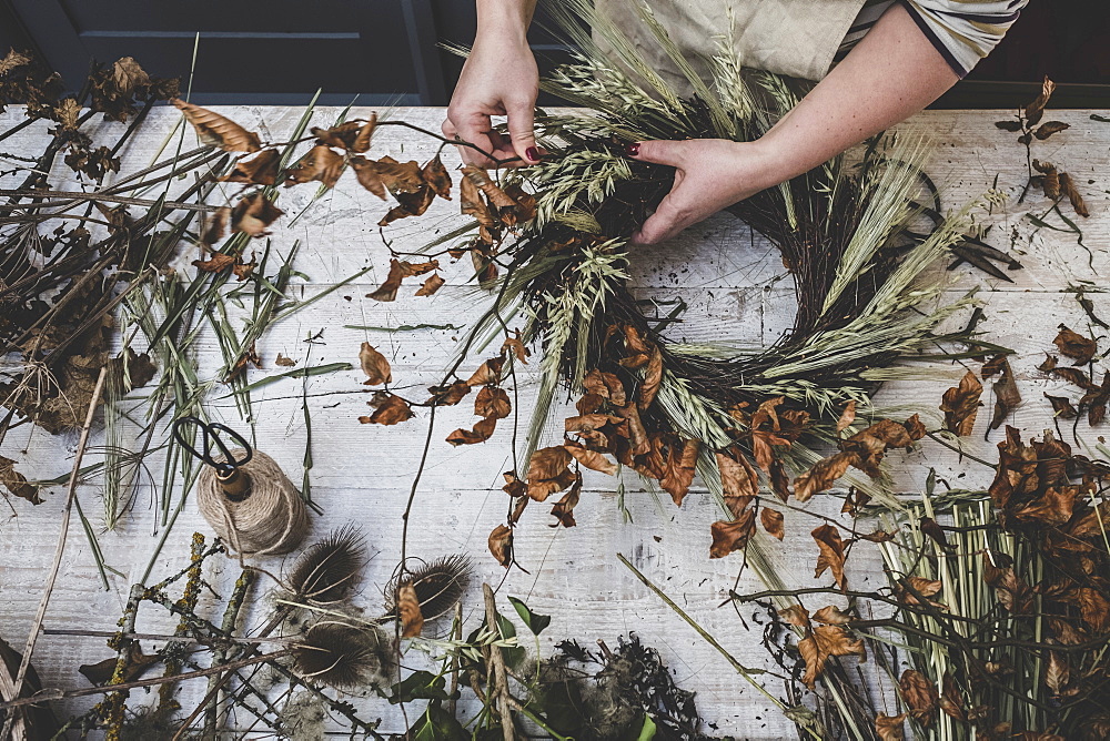 Woman making a small winter wreath of dried plants, brown leaves and twigs, and seedheads