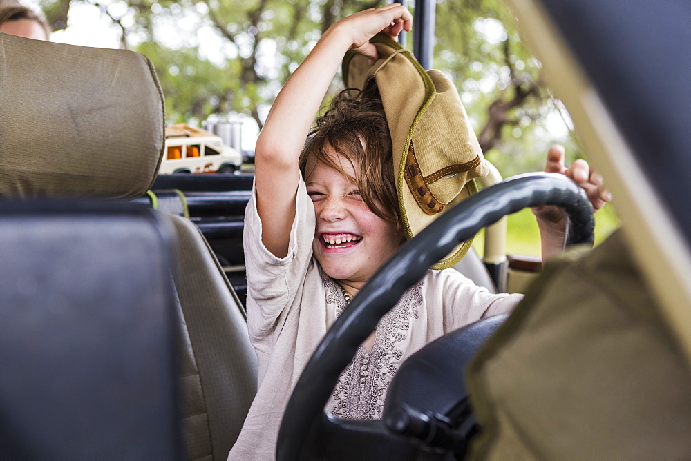 Portrait of smiling Six year old boy with a large hat in the driving seat of a safari vehicle