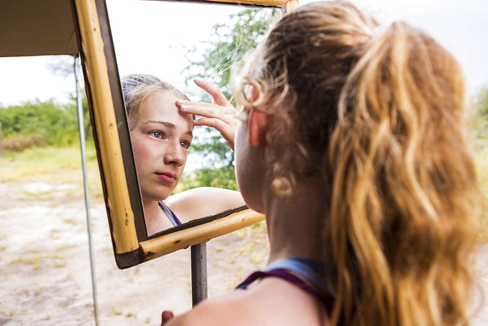 Thirteen year old girl looking into mirror at a tented camp, applying sunscreen to her forehead