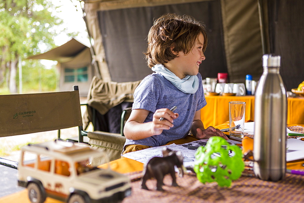 Smiling boy, profile, in a tented camp, on safari, playing with safari animal toys