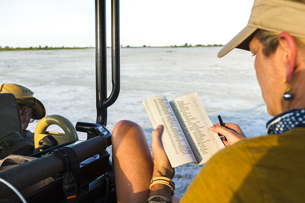 A woman looking at a book or journal in a safari vehicle, Botswana