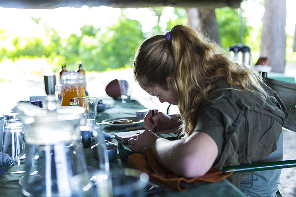 Thirteen year old girl writing in her journal, tented camp, Botswana