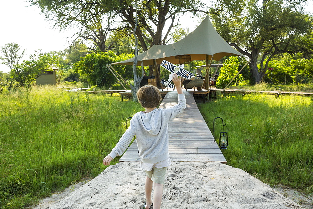 Six year old boy playing with toy airplane, tented camp, Botswana