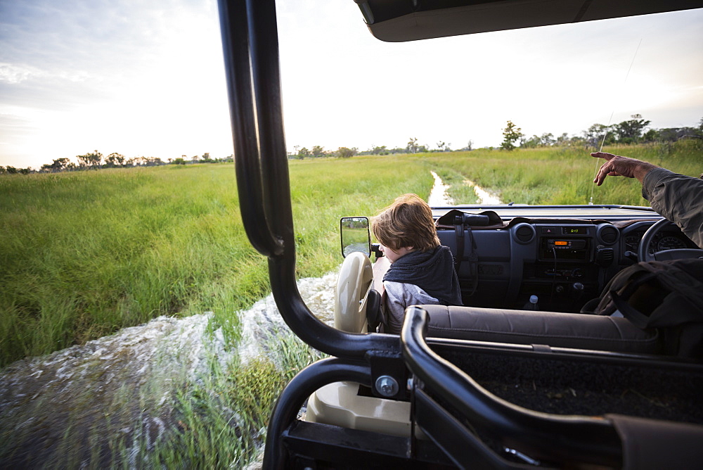 A six year old boy riding in safari vehicle looking out over the landscape, Botswana