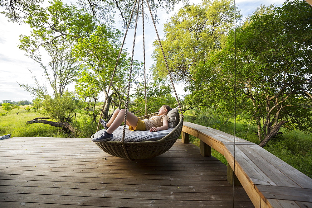 Thirteen year old girl resting in large swing on a deck at a safari camp, Botswana