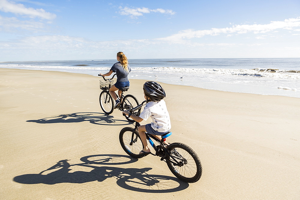 Children cycling on the sand by the water, a boy and girl, United States of America