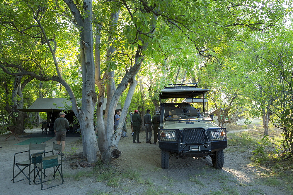 Safari vehicles and guides under the trees in a wildlife reserve camp, Okavango Delta, Botswana