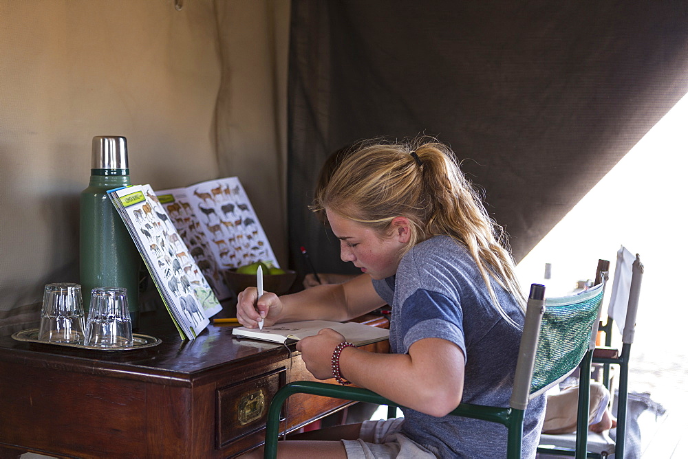 Twelve year old girl seated in a tent, writing or drawing in a journal