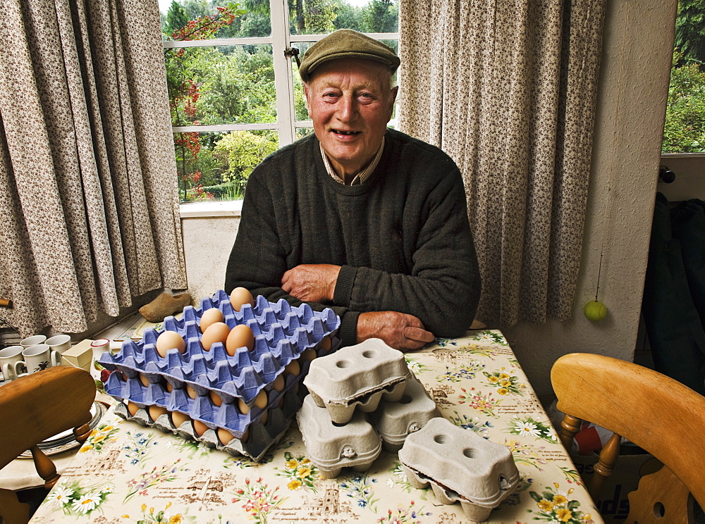 A farmer seated at a table in a farmhouse with trays of fresh eggs, Gloucestershire, England