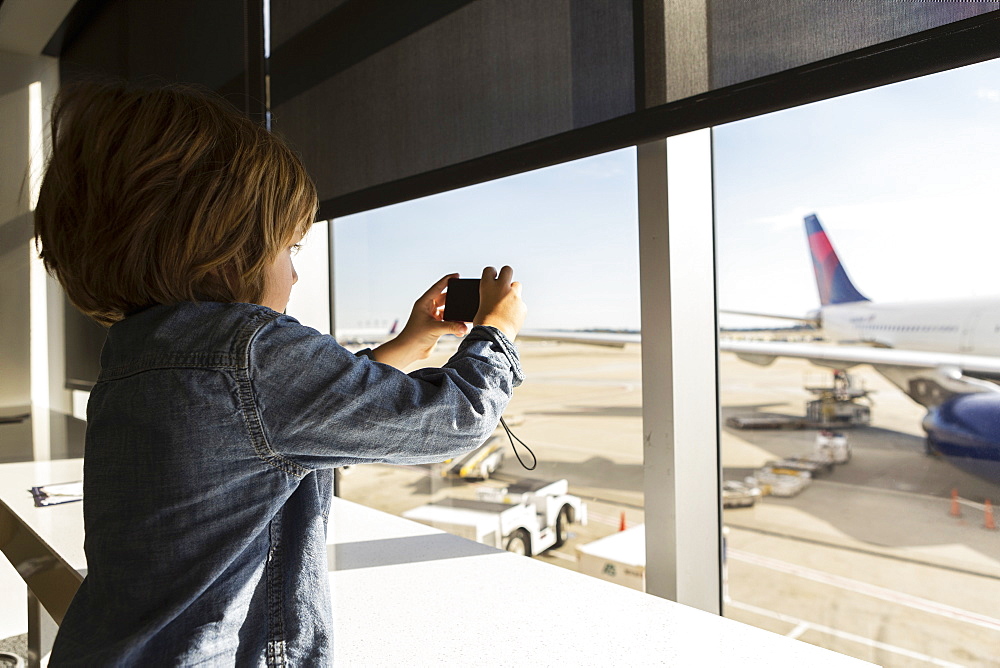 A five year old boy taking a photograph of airplane from an airport departure lounge