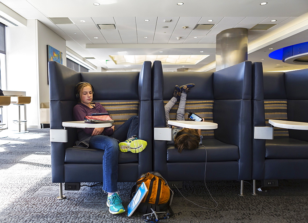 Two children watching their digital tablets, awaiting a flight in an airport departure lounge