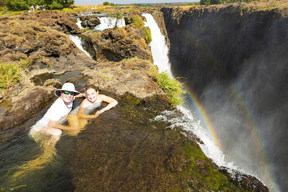 Mature man and girl, father and young teenage daughter in the water at the Devils Pool, on the cliff top overlooking Victoria Falls, Zambia