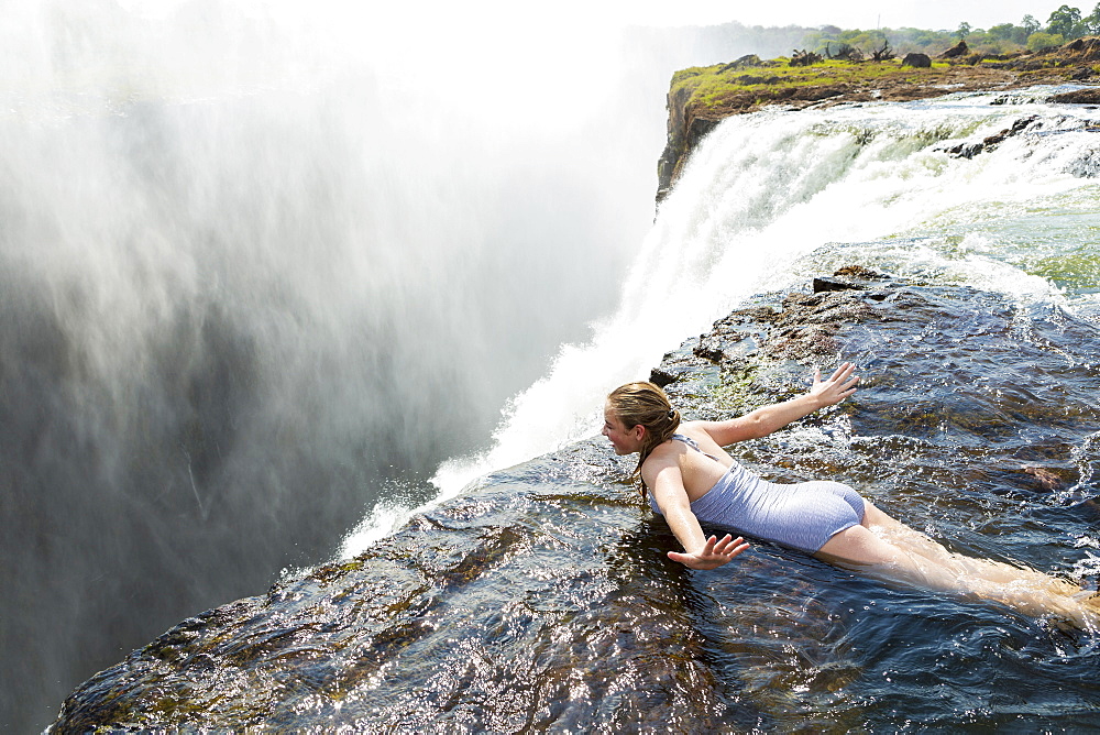 Young girl in the water at the Devils Pool lying on her front, arms spread out, at the edge of the cliff of Victoria Falls, Zambia