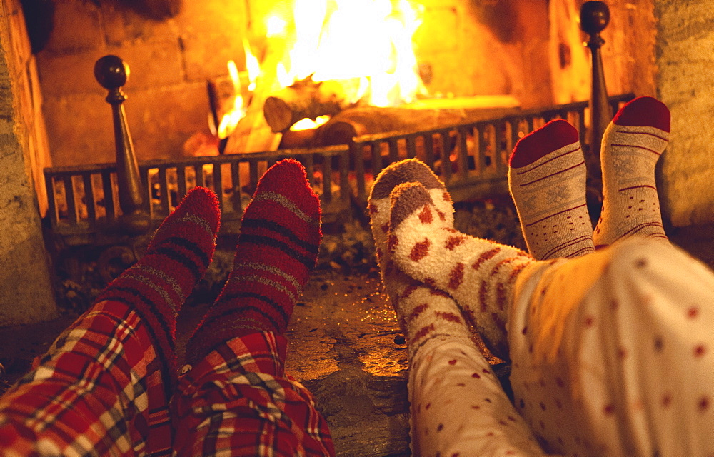 Legs and feet of three people wearing pyjamas and warm socks lying in front of a fireplace