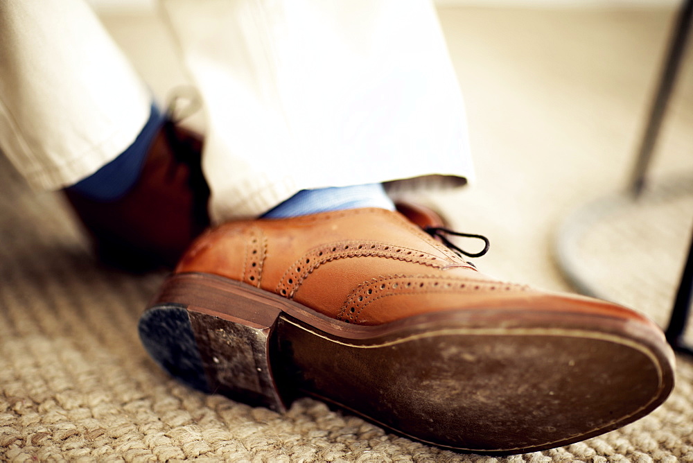 Close up of person's feet, wearing brown leather brogues, blue socks and white trousers