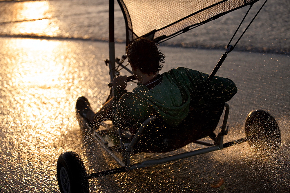 Rear view of person riding a sand yacht along a sandy beach at sunset