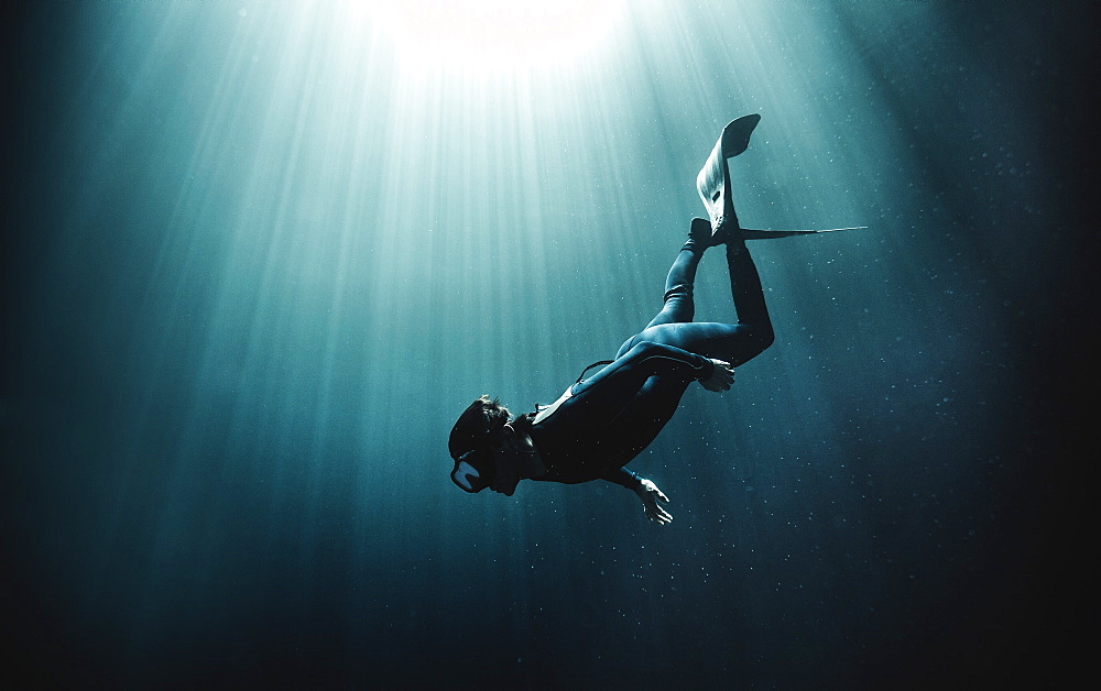 Underwater view of diver wearing wet suit and flippers, sunlight filtering through from above, United States of America