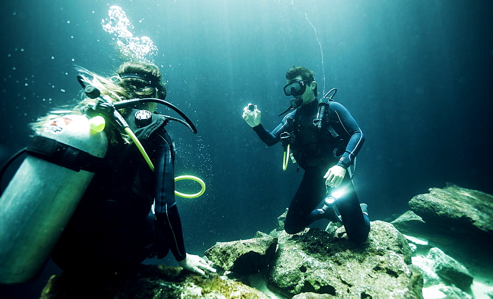 Underwater view of two divers wearing wetsuits, diving goggles and oxygen cylinders, United States of America