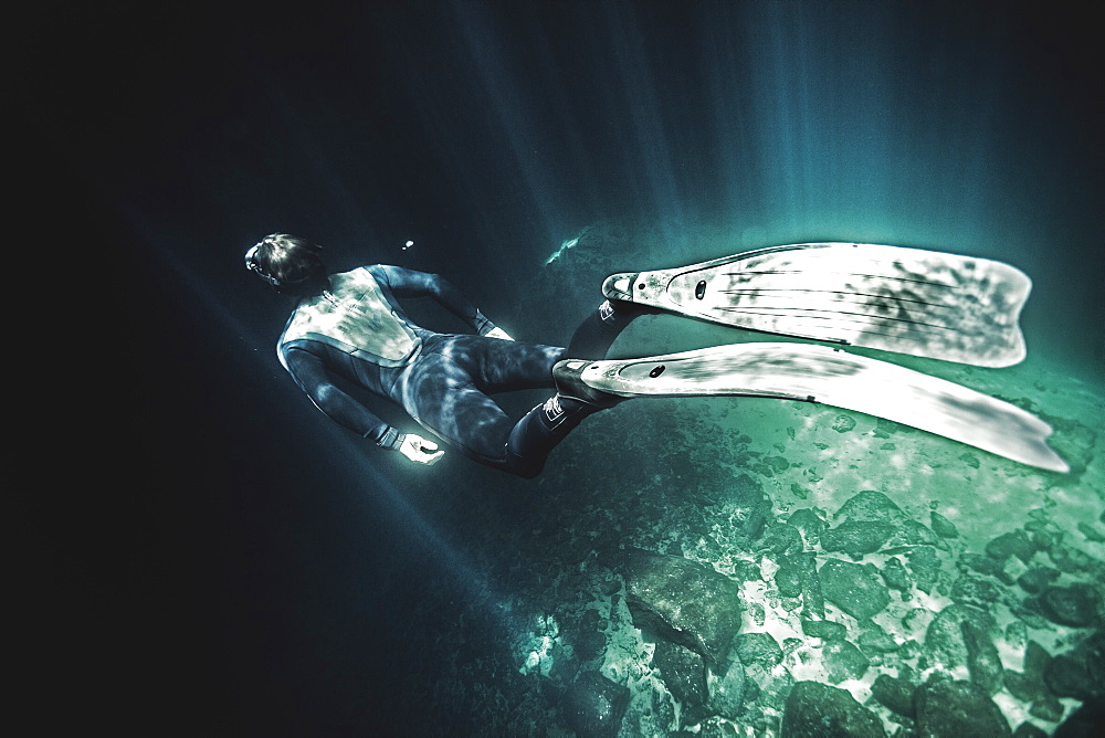 High angle underwater view of diver wearing wet suit and flippers, sunlight filtering through from above, United States of America