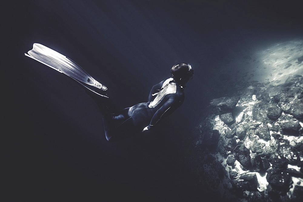 Underwater view of diver wearing wet suit and flippers, diving near rocks, United States of America