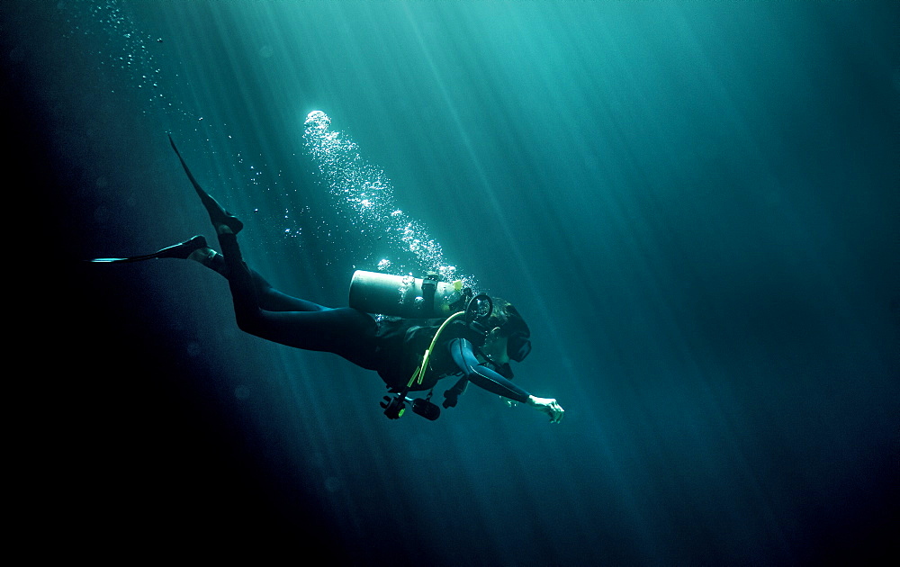 Underwater view of diver wearing wetsuit, diving goggles and oxygen cylinder, air bubbles rising, United States of America