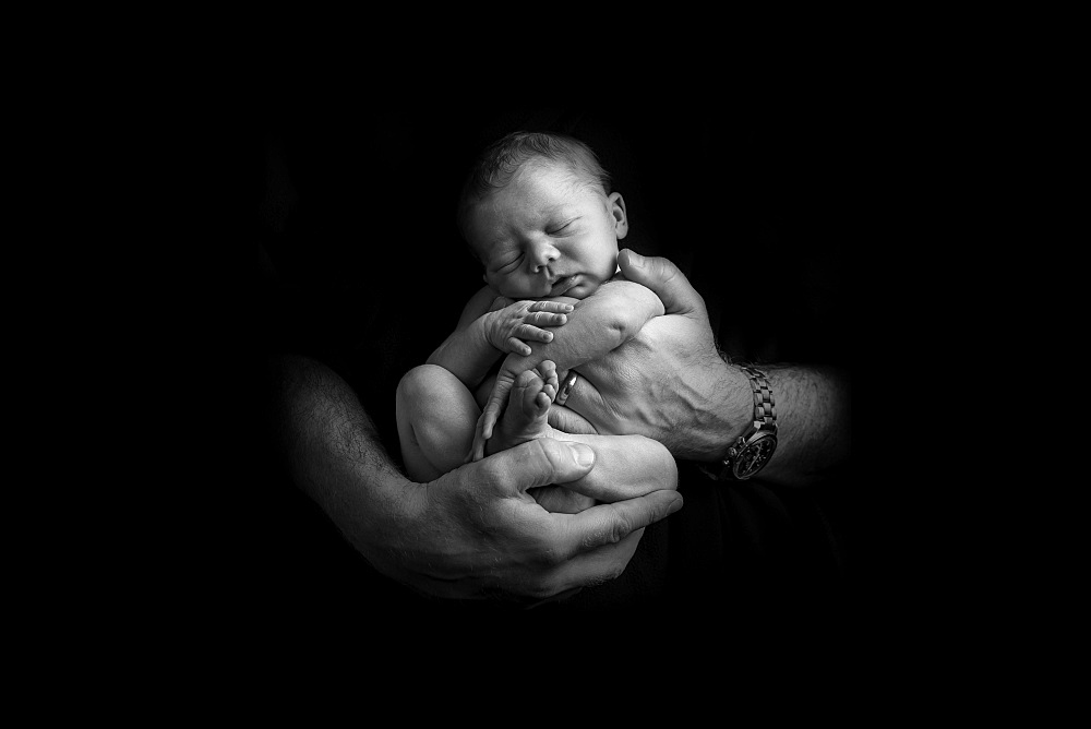 Sleeping newborn baby being held in hands of father