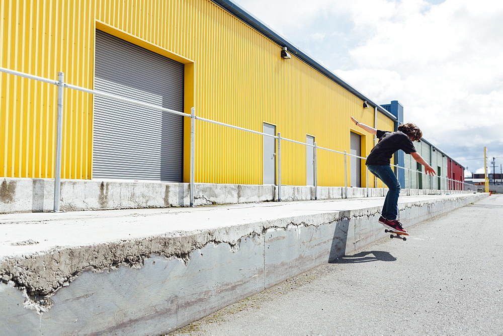 Teenage boy skateboarding in front of industrial warehouse loading zone