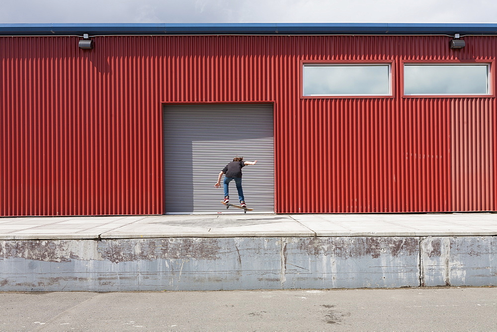 Teenage boy skateboarding in front of industrial warehouse loading zone