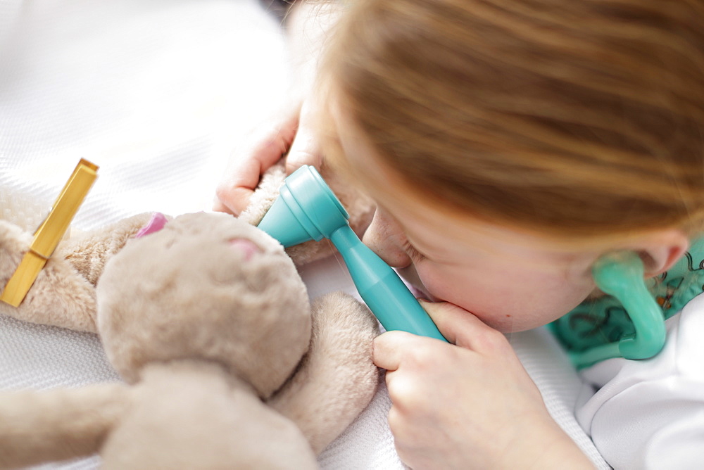 Young girl dressed as doctor pretending to treat toy animal in make-believe hospital bed