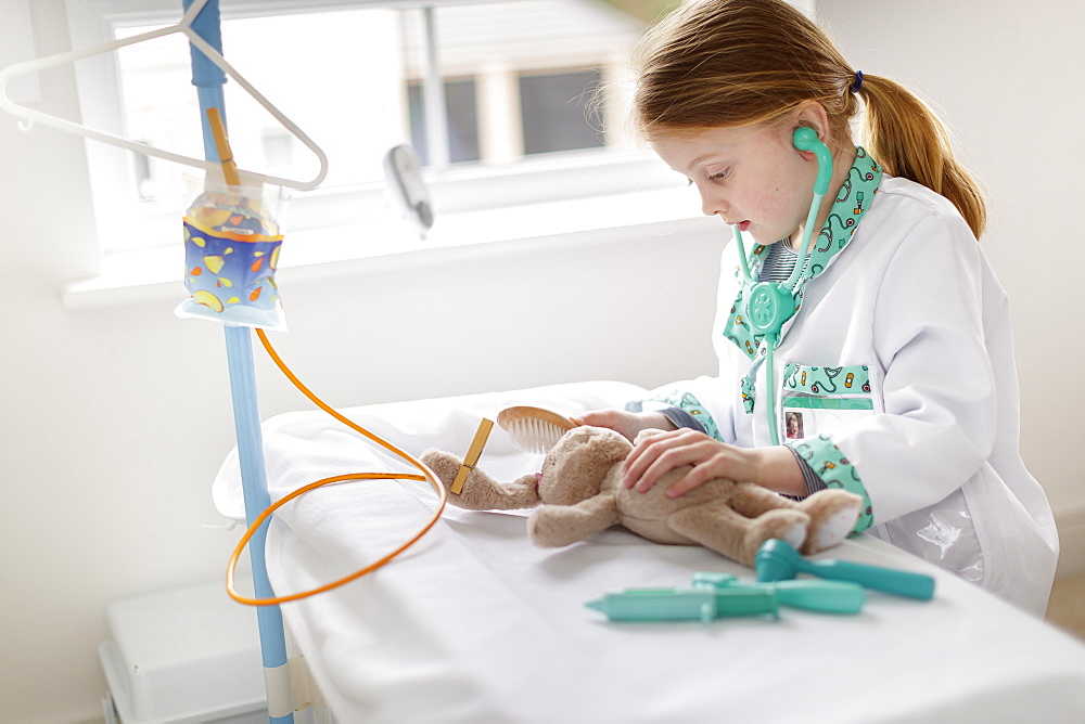 Young girl dressed as doctor pretending to treat cuddly animal in make-believe hospital bed