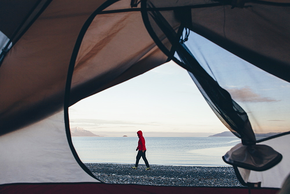 View through doorway of camping tent of woman walking on beach Muir Inlet in distance, Glacier Bay National Park, Alaska