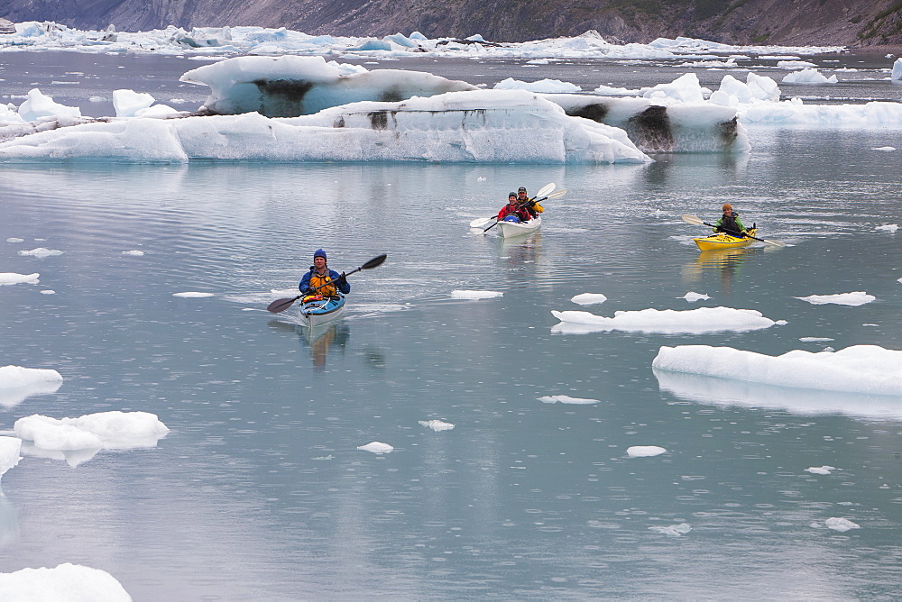 Sea kayakers paddling in glacial lagoon at a glacier terminus on the coast of Alaska