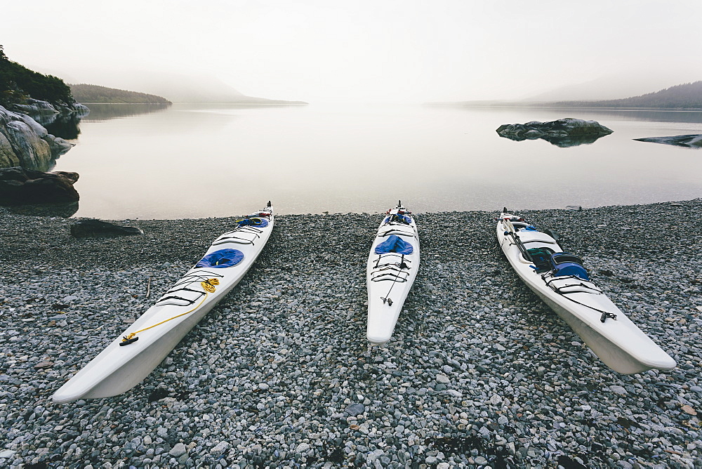 Three sea kayaks pulled up into shoreline of secluded cove in Muir Inlet overcast sky in distance, Glacier Bay National Park, Alaska