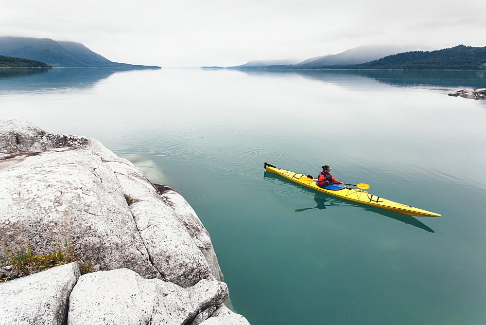 Female sea kayaker paddling pristine waters of Muir Inlet overcast sky in distance, Glacier Bay National Park, Alaska