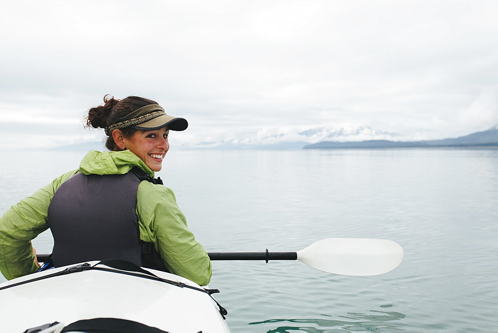 Happy female woman sea kayaking pristine waters of Muir Inlet, Glacier Bay National Park and Preserve, Alaska