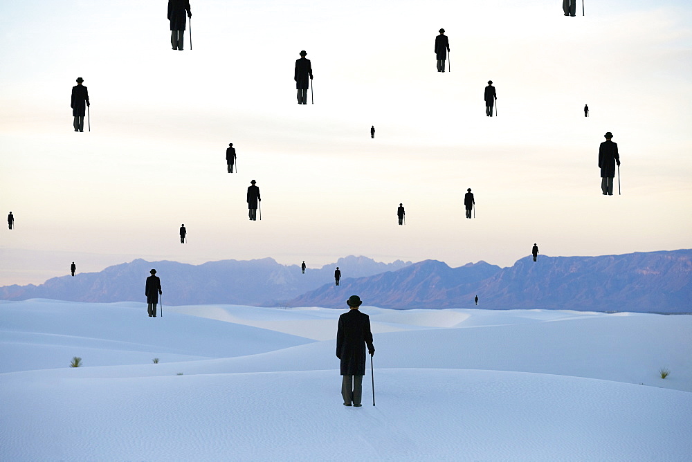 Men in bowler hats with umbrellas outline of figures floating above ground in a sand dune desert