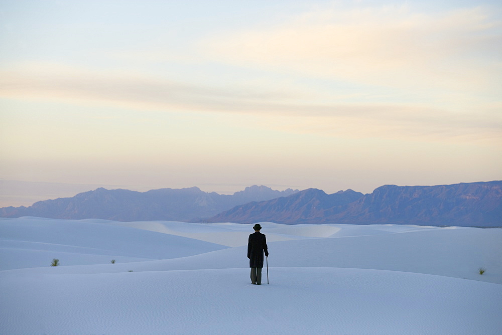 Man in a black coat and suit a bowler hat and umbrella in a white desert wilderness of white sand