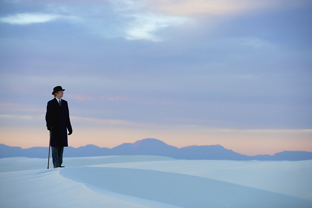 Man in a black coat and suit a bowler hat and umbrella in a white desert wilderness of white sand