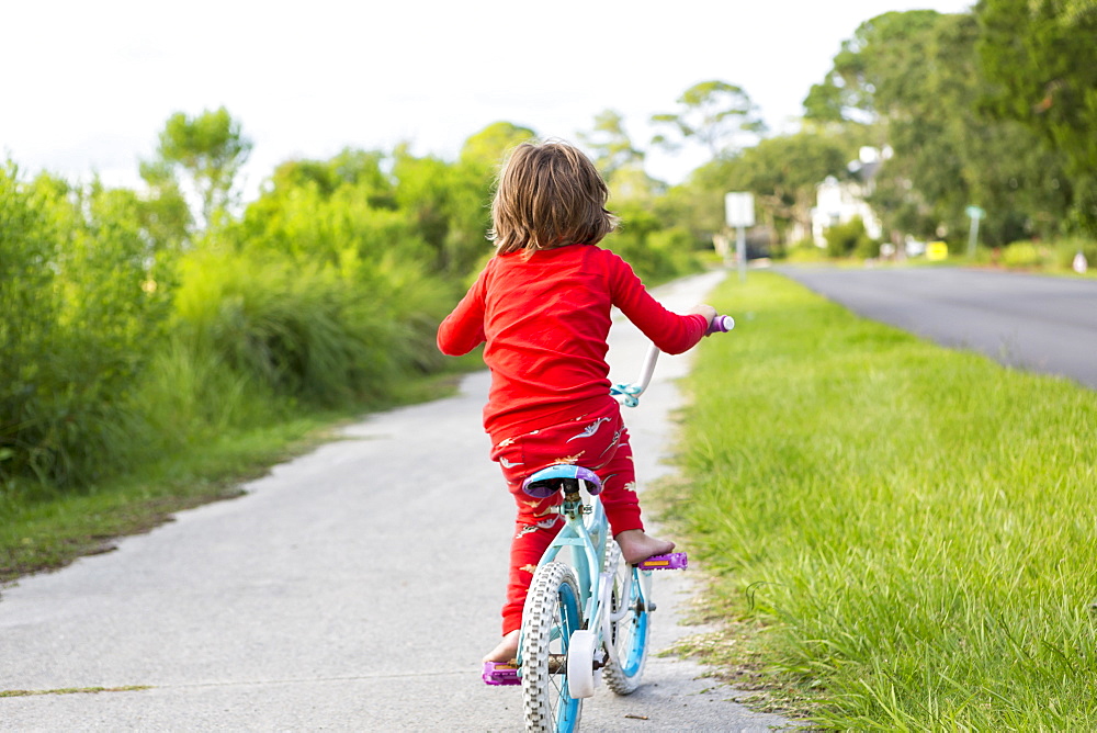 A five year old boy in a red shirt riding his bike on a quiet residential street