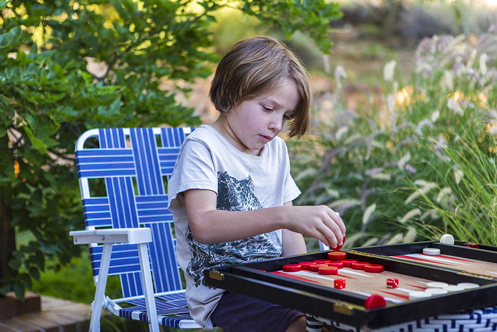 A young boy playing backgammon outdoors in a garden, New Mexico, United States