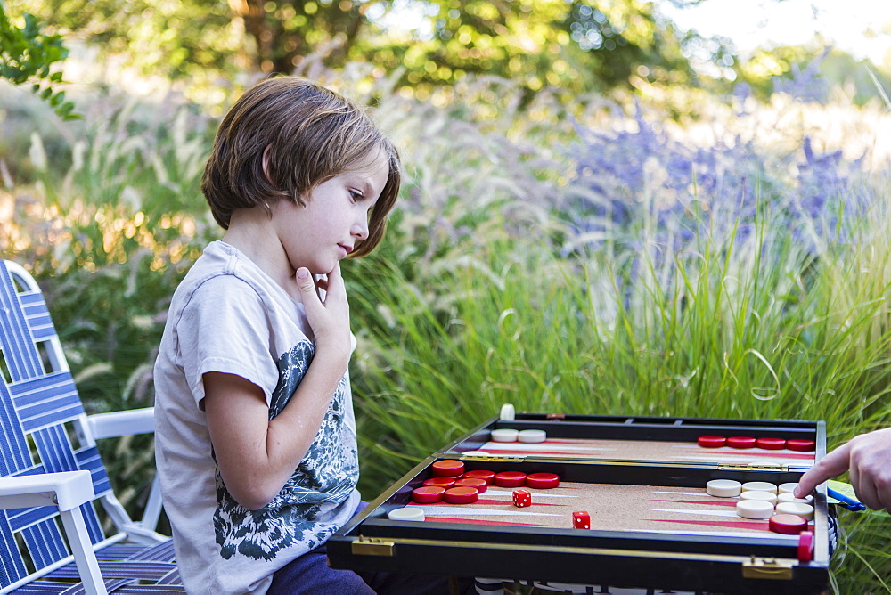 A young boy playing backgammon outdoors in a garden, New Mexico, United States