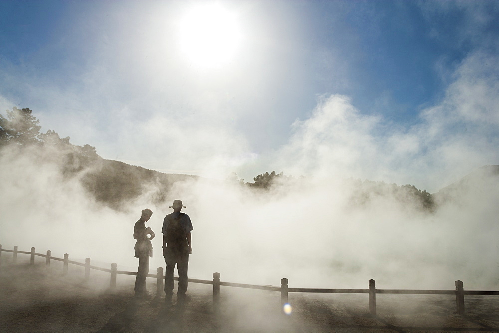 Two people in rising mist at a thermal pool site, Rotorua, North Island, New Zealand