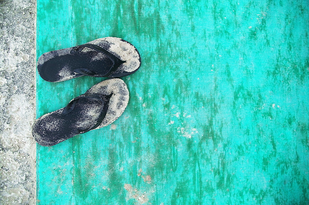 High angle close up of sandy black flip flops on turquoise floor mat