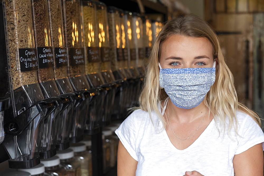 Portrait of young blond woman wearing face mask, standing in waste free wholefood store, Watlington, Oxfordshire, United Kingdom